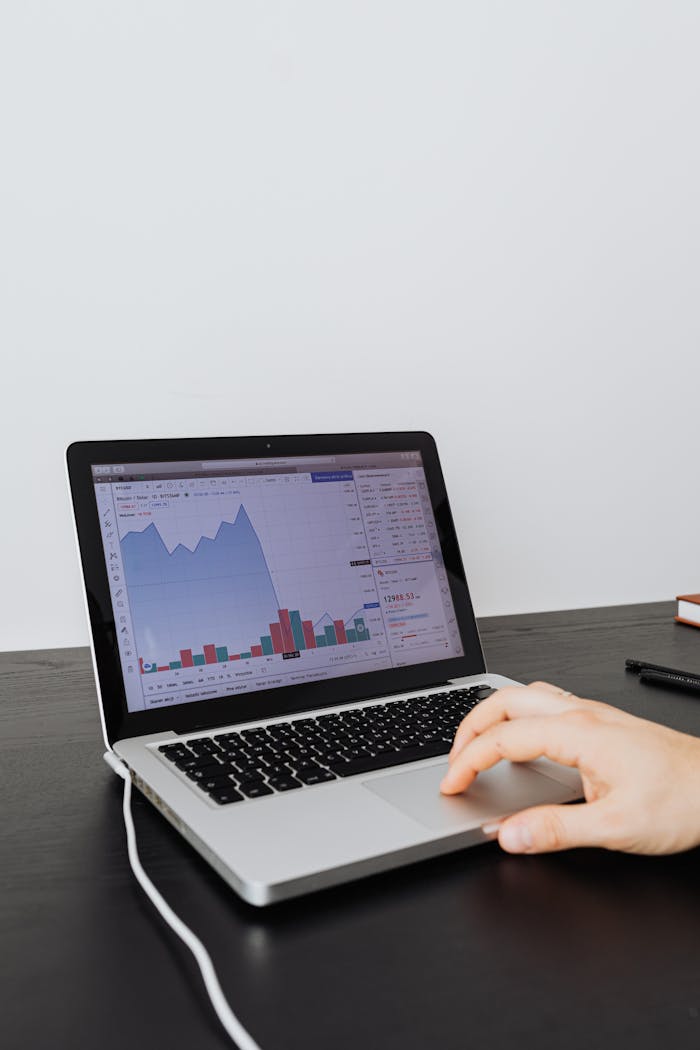 Person analyzing financial data on a laptop indoors, focusing on graphs and charts.